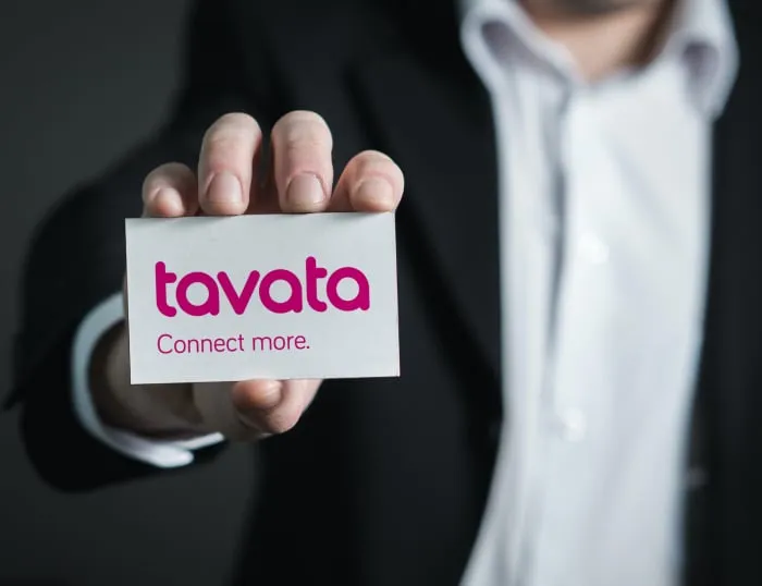 A person in a suit holding out a Tavata business card