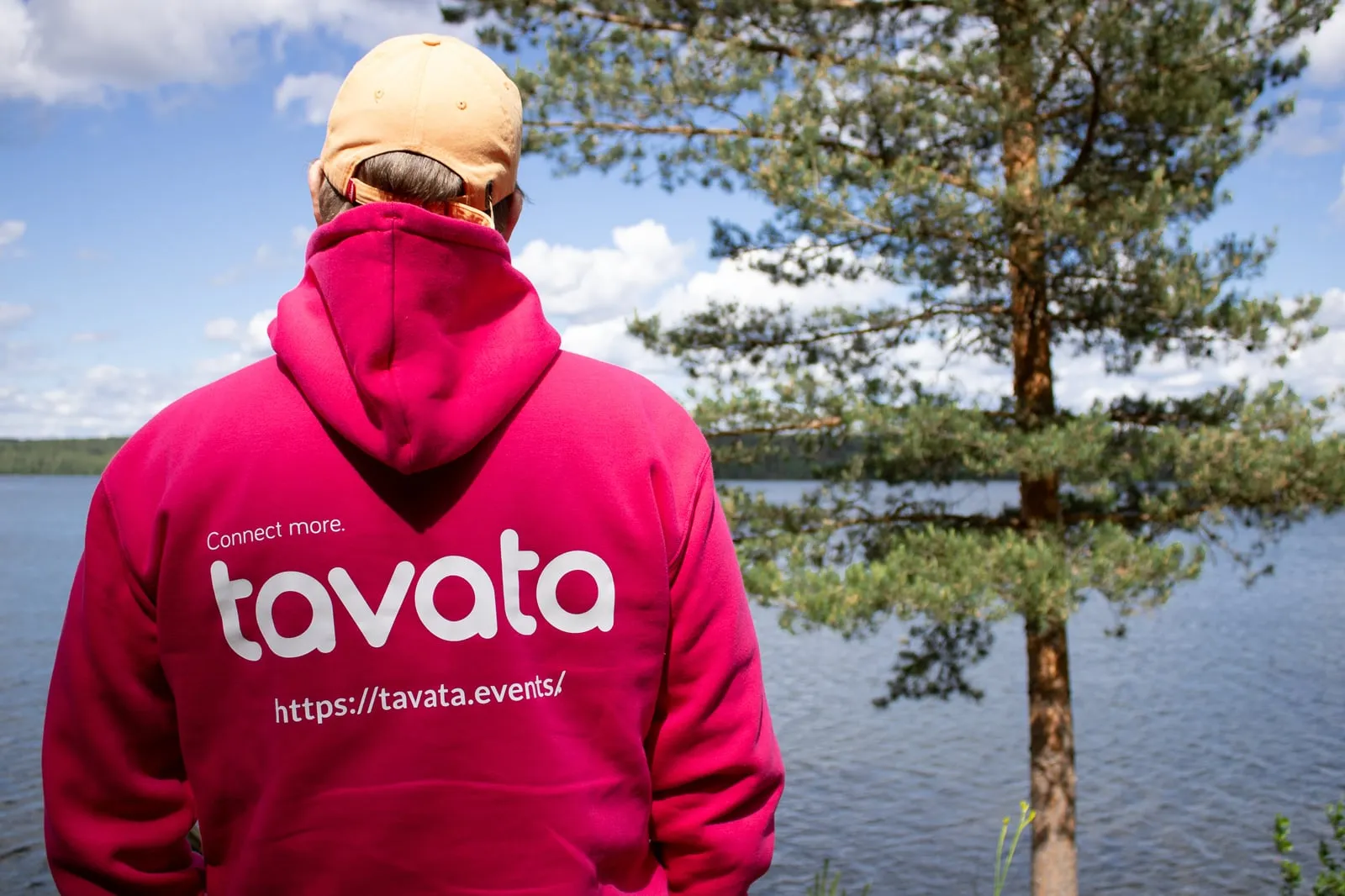 A person in a pink Tavata hoodie looking out over a lake