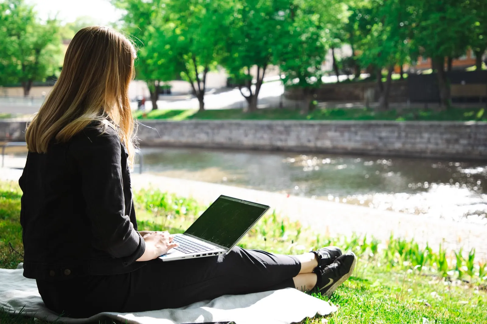 A woman working on a laptop on the grass by a river