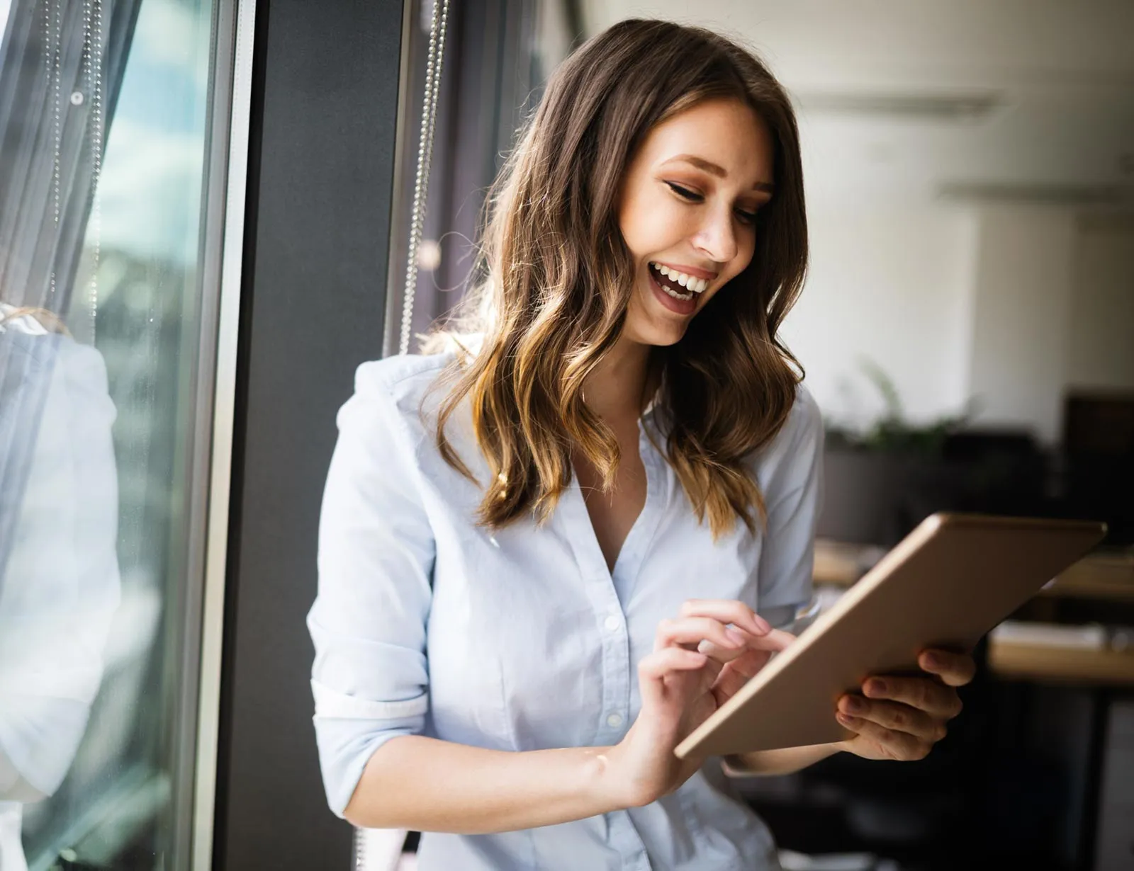A smiling woman using a tablet by an office window